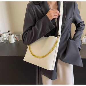 Close-up of a white leather bucket bag with a bold gold chain and adjustable strap
