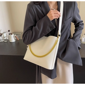Close-up of creamy white leather tote bag with thick gold chain and wide shoulder strap