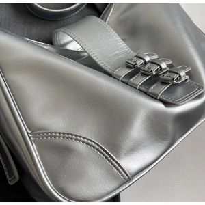 Detail of silver metallic handbag featuring triple buckled straps and premium stitching