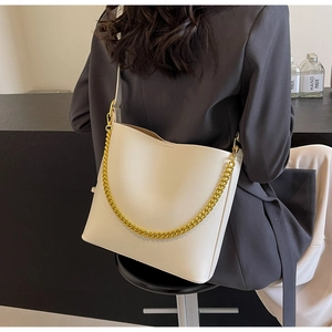 Close-up of cream leather tote bag with thick gold chain and crossbody strap on model