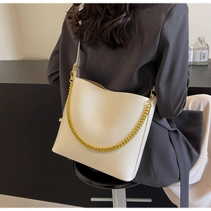 Detail of off-white leather bucket bag with chunky gold chain strap worn by a model