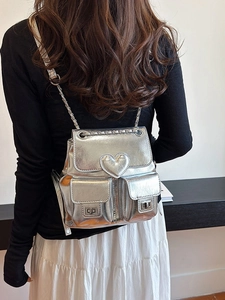 Silver metallic backpack with heart detail and chain straps shown on a model