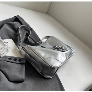 Detail of silver metallic shoulder bag featuring decorative buckles on grey suit background