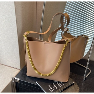 Detailed shot of beige leather tote bag with thick gold chain handle on minimal desk