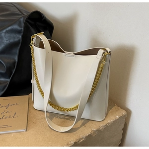 Detail of cream white tote bag with chunky gold chain strap and leather handle on stone surface