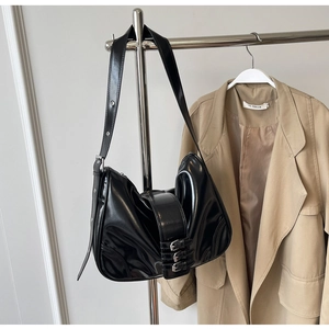 Detailed close-up of glossy black patent leather hobo bag with silver metal buckles