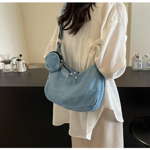 Dettaglio di una borsa hobo in denim blu con un mini portamonete rotondo abbinato sulla tracolla