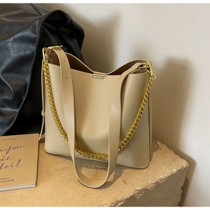 Detail view of cream bucket bag with wide leather strap and gold chain on stone
