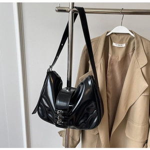 Detail of black glossy crescent hobo bag with three decorative metal buckle straps