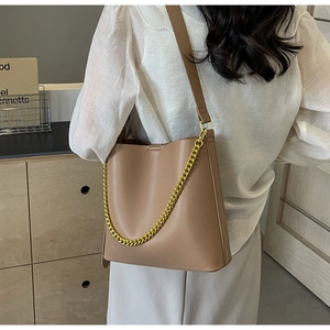 Model wearing tan matte leather tote bag with gold chain strap in a minimalist setting