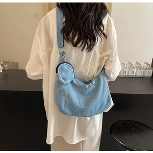 Detail view of light blue denim crossbody bag with round coin purse on casual model