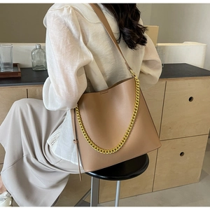 Brown leather tote bag with thick gold chain detail worn by model in minimalist setting