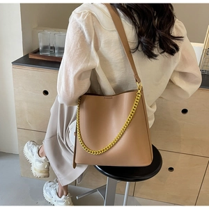 Detail of camel leather tote bag with gold chain strap shown on person in white shirt