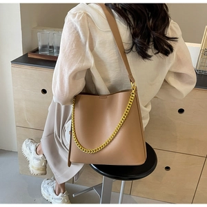 Brown leather tote bag with chunky gold chain detail shown on shoulder of a model