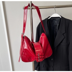 Detail view of glossy red shoulder bag with three silver buckle straps on a hanger