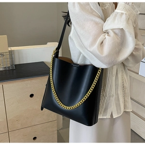Detail of black leather bucket bag with gold chain and shoulder strap shown on model
