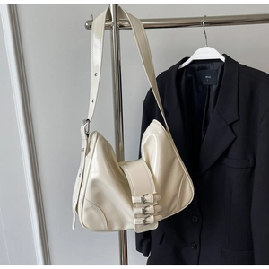 Detail view of cream patent leather shoulder bag featuring triple silver buckle straps decoration