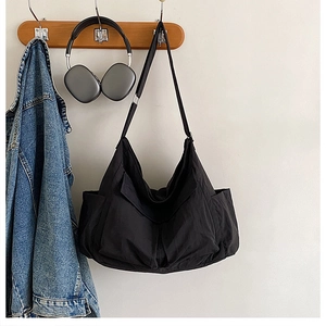Detail of black utility canvas crossbody bag hanging with headphones on wood hook