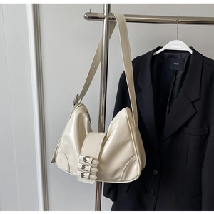 Detail showing the cream faux leather texture and triple silver buckles of the shoulder bag