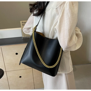 Detail of a large black leather tote bag featuring a decorative gold chain and strap