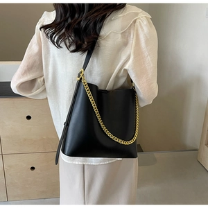 Shoulder view of a black leather tote bag with a decorative chunky gold chain accent