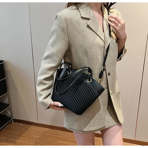 Detail of black pleated tote bag with golden hardware shown on a model in beige dress