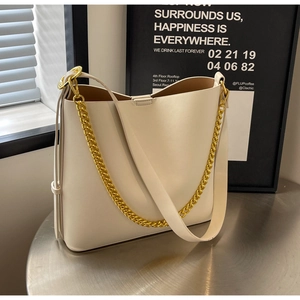 Detail of cream tote bag with gold chain strap and spacious interior on metallic desk