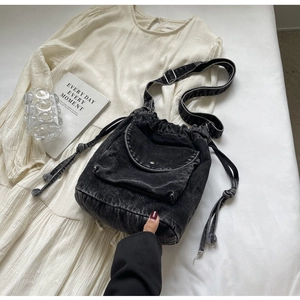 Details der schwarzen Denim-Beuteltasche mit Kordelzug und Metallschnalle auf weißem Kleid