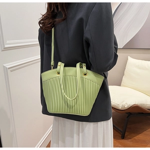 Detail of light green pleated crossbody bag with gold hardware on a gray blazer