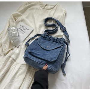 Detail der blauen Denim-Beuteltasche mit Kordelzug und Silberschnalle auf weißem Kleid