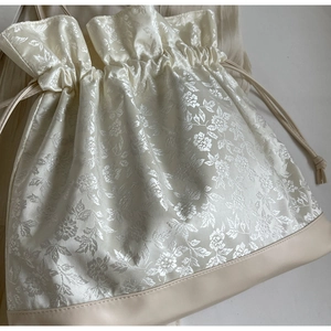 Detail of floral jacquard fabric and matte faux leather base on beige drawstring bag