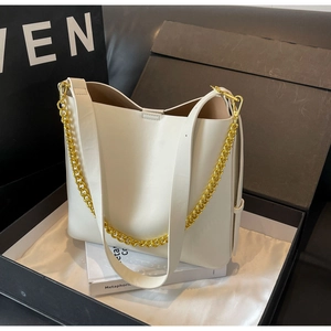 Detail of a creamy white tote bag with a golden chain strap in a premium gift box