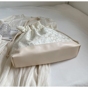 Detail of cream white drawstring tote bag featuring floral jacquard and leather texture