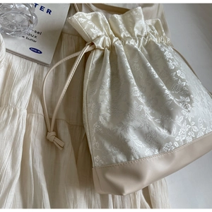 Detailed view of cream jacquard floral fabric drawstring bag with faux leather base
