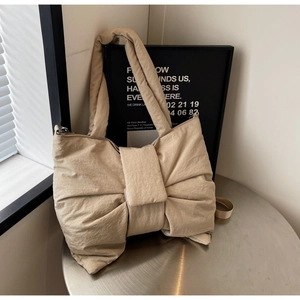 Sac cabas matelassé beige en nylon avec grand nœud exposé sur une table argentée
