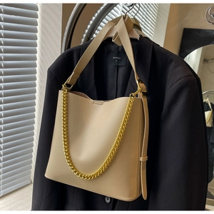 Detail of beige leather tote bag with thick gold chain on a black blazer jacket