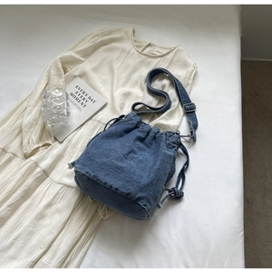 Detail der blauen Denim-Beuteltasche mit Kordelzug auf weißem Plissee-Kleid