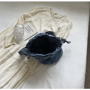 Flatlay der blauen Denim-Beuteltasche mit Kordelzug und einem cremefarbenen Oberteil