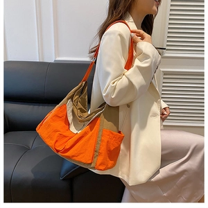 Detail view of large canvas crossbody bag in orange and khaki colors worn by model
