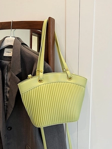 French retro pleated straw tote bag in light green with golden metal rings on a wooden rack