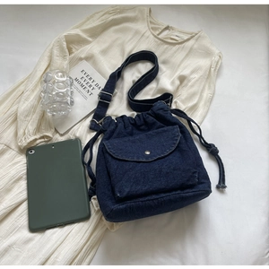 Flachbild einer blauen Denim-Beuteltasche mit Kordelzug und Metallknopftasche auf strukturiertem Stoff