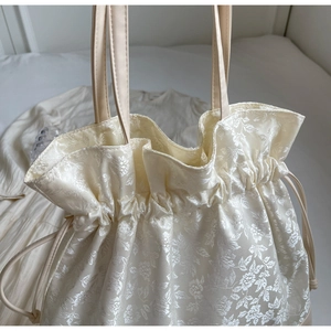 Close-up of cream floral jacquard drawstring tote bag with ruffled edge details