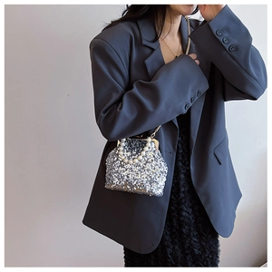 Silberne Pailletten-Tasche mit Perlengriff und Kette getragen über grauem Blazer