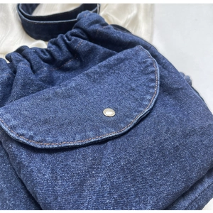 Detail eines dunkelblauen Denim-Rucksacks mit Kordelzug, Ziernähten und Druckknopf