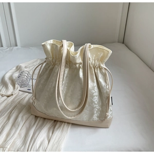 Detail of beige jacquard drawstring bucket bag with retro floral pattern and leather base