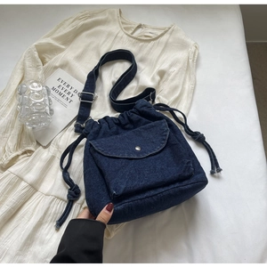 Nahaufnahme einer tiefblauen Denim-Umhängetasche mit Kordelzug und vorderer Klappentasche