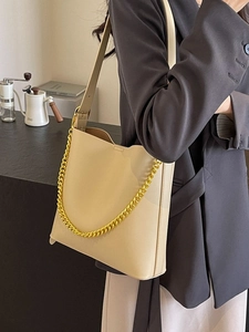 Large beige tote bag with gold chain and shoulder strap worn by model in business attire