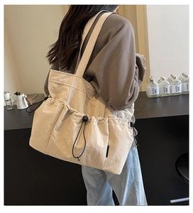 Side view of large cream canvas tote bag with drawstrings and multi-pocket design on model
