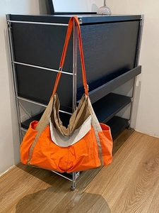Large orange and khaki canvas crossbody bag with adjustable strap on a modern metal rack