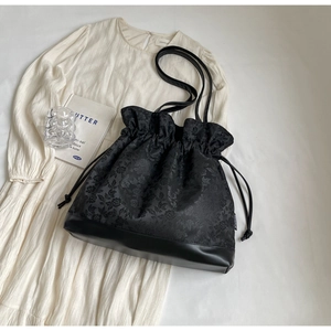 Detail of floral jacquard fabric and leather stitching on black drawstring tote bag